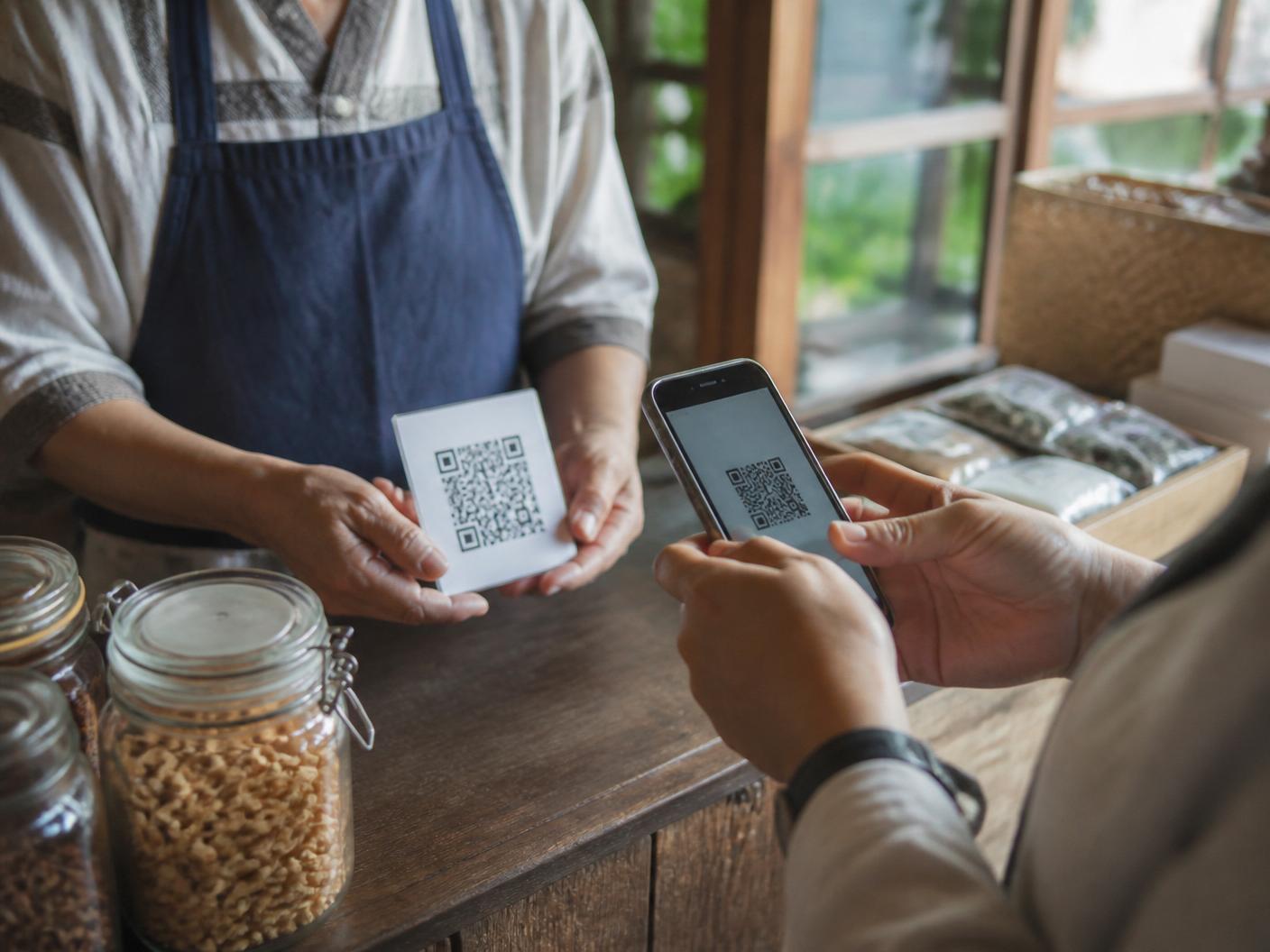 Merchant and customer completing a QR code payment at a shop counter